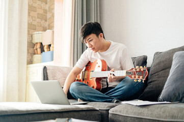 Young Asian man learning guitar with laptop