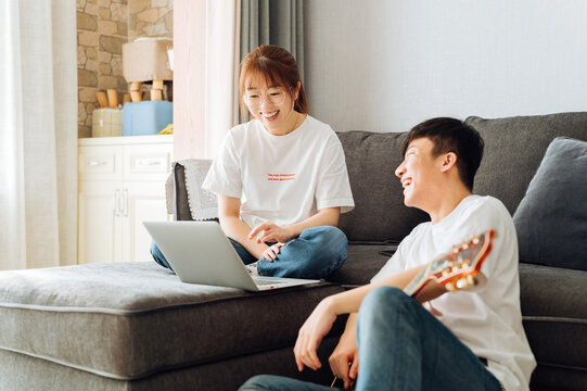 Young man playing guitar while his girl friend working at home