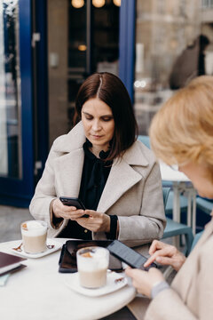 Women using smartphones at table with coffee on terrace