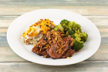 Beef brisket slices with barbecue sauce, mashed potatoes with cheese and spicy broccoli on white plate
