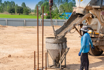 Workers load cement concrete from truck to bucket for pouring on formwork.
