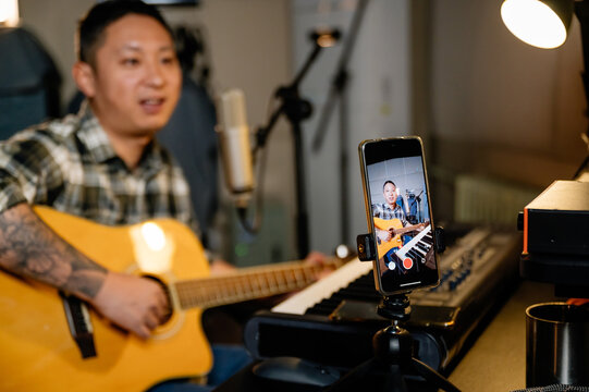 Man playing guitar in his studio and recording by phone