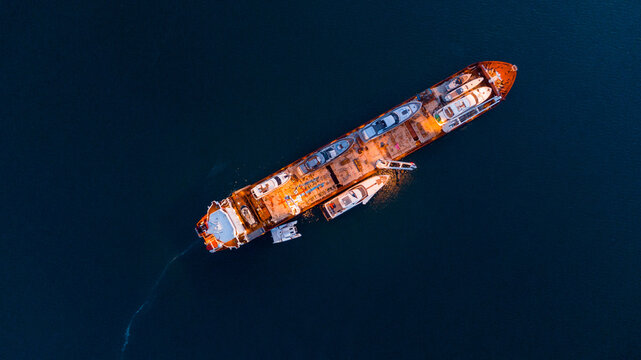 drone overhead of a Cargo transporter with yachts at night 