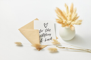 Envelope with greeting card near vase with dry wheat ears