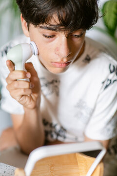 Teenager cleaning face with electric brush
