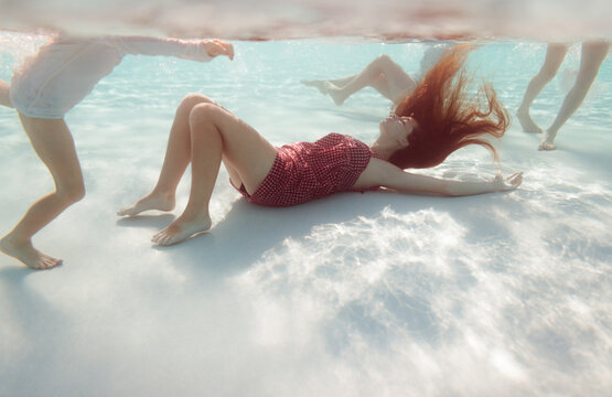 Woman lying on the bottom of the pool surrounded by kids