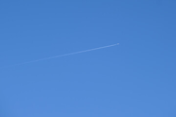 Distant passenger jet plane flying on high altitude on clear blue sky leaving white smoke trace of contrail behind. Air transportation concept