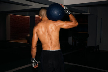 View of the back of a strong man holding a fitness ball 