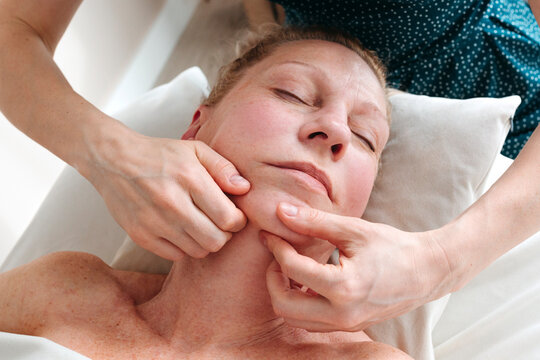 Female hands massaging face of senior woman.