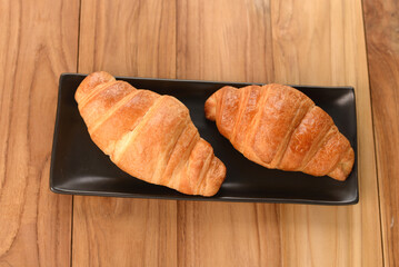 croissant on black saucer on wooden table topview