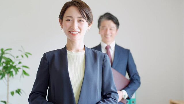 オフィス内でカメラを見て微笑むスーツを着た日本人男女