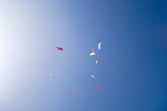cluster of colourful paragliders in a blue sky