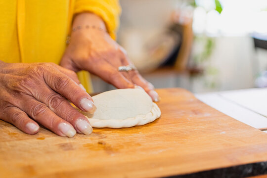 Hands kneading flour to make empanadas on a wooden chopping board