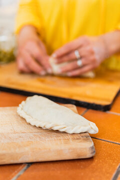 Hands kneading flour to make empanadas on a wooden chopping board
