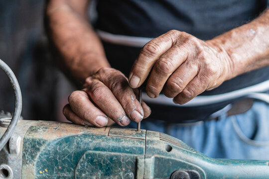 Hands of an old man repairing a machine