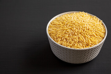 Raw Organic Risoni Pasta in a Bowl on a black background, side view. Copy space.