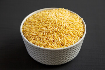 Raw Organic Risoni Pasta in a Bowl on a black background, side view.