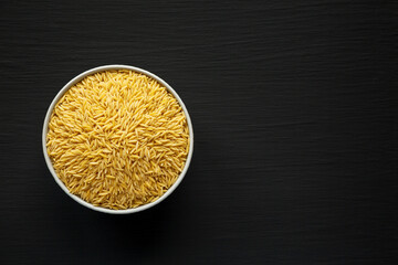 Raw Organic Risoni Pasta in a Bowl on a black background, top view. Flat lay, overhead, from above....