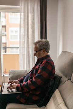 Senior man typing on laptop sitting on sofa