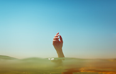 Human hand emerging from the sea on a sunny day