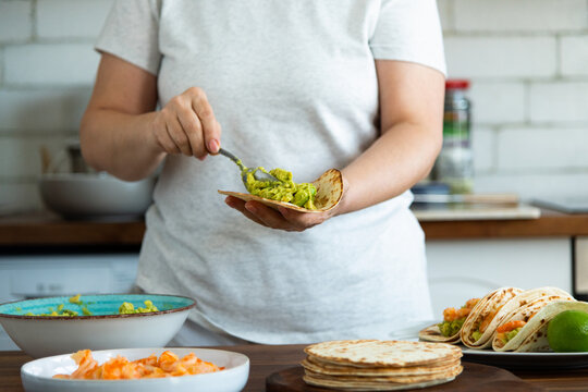 Preparing shrimp tacos: woman placing avocado guacamole on tortilla 