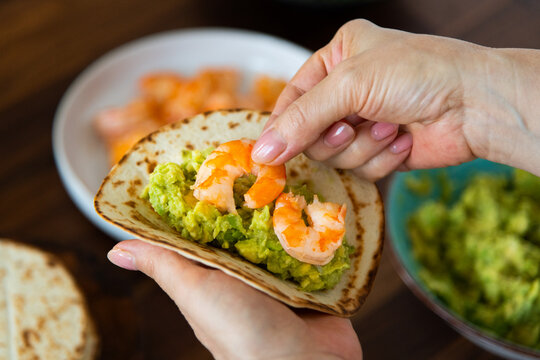 Preparing shrimp tacos: woman placing shrimps on tortilla 