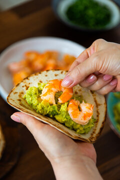 Preparing shrimp tacos: woman placing shrimps on tortilla 