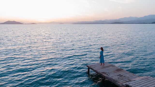young woman standing on the dock watching sunset