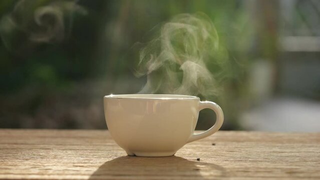 Cup of hot coffee or tea with steam on wood table in morning. Nature background in sunshine. Hot coffee or tea concept.