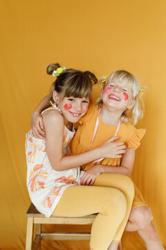 Portrait of two little girls over yellow backdrop in yellow outfit