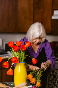 Grey-haired senior cutting off colorful flowers at home 