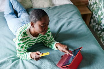 Young woman lying on her bed and shopping online