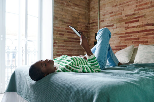 Young woman lying on her bed with an e-reader