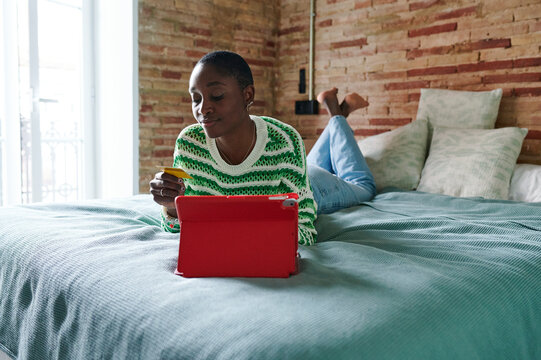 Young woman shopping online while lying on her bed