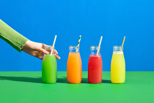 Female hand with bottles of juices on color background