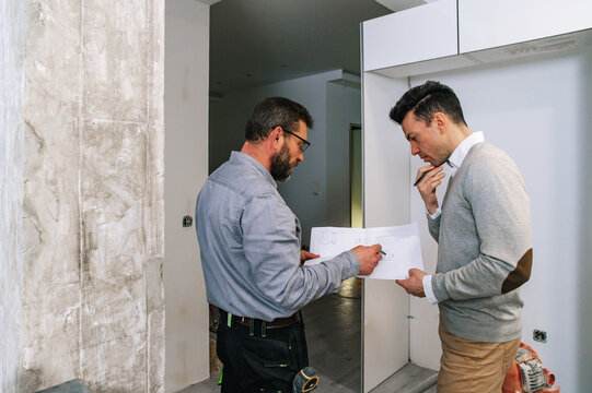 Men with draft examining apartment wall