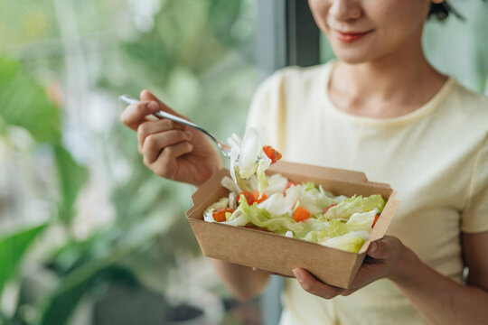 thoughtful asian woman holding box of green salad