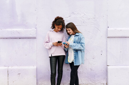 Teen girls standing outside on a sidewalk with smartphones