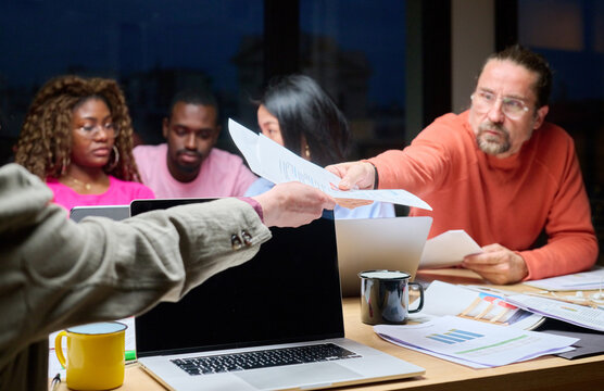 Coworkers passing document at desk.