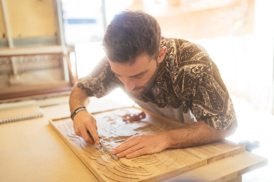 Focused guy carving wood with chisel in joinery