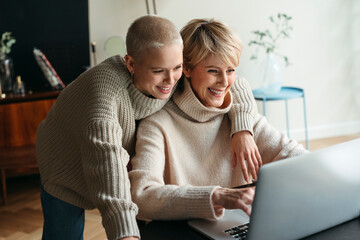 Happy mother and adult daughter using electronic device.