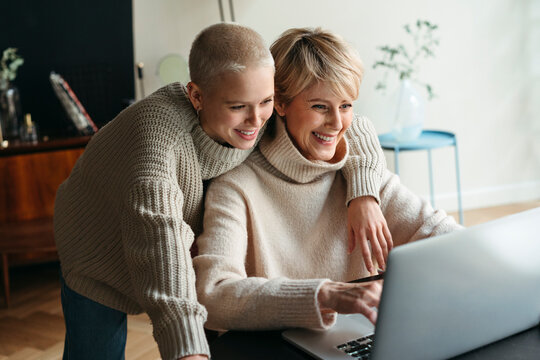 Happy mother and adult daughter using electronic device.