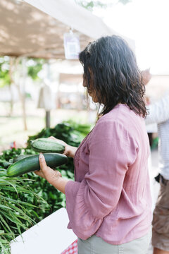 Woman choosing between various cucumbers