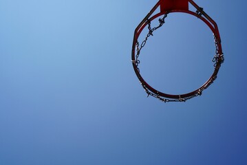 Fototapeta na wymiar View from below of basketball basket with chains and rusty red hoop with cloudless blue sky background, motivation to do sports outdoors, new goals concept