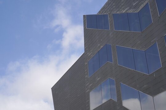 View from below of modern building with windows reflecting the blue sky in the background, with small white clouds, copy space