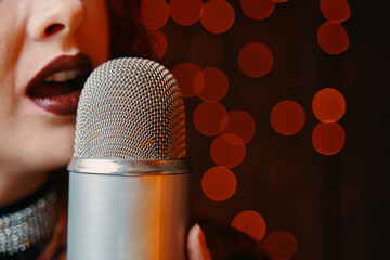 Woman singer with disco mic on bokeh light background. Close-up of female's lips painted with burgundy lipstick and retro microphone. Redhead girl starting concert. Copy space for gig posters.