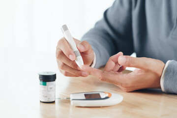 Asian man using lancet on finger for checking blood sugar level by Glucose meter, Healthcare and Medical, diabetes, glycemia concept