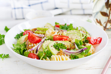 Fusilli pasta salad with avocado, tomatoes, fresh green lettuce, red onion and mustard dressing on white background. Vegetarian healthy lunch.