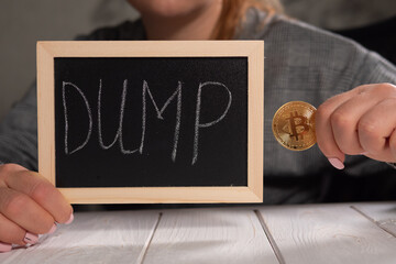 Close-up of a woman holding a board with the inscription DUMP and a golden bitcoin coin. Falling...