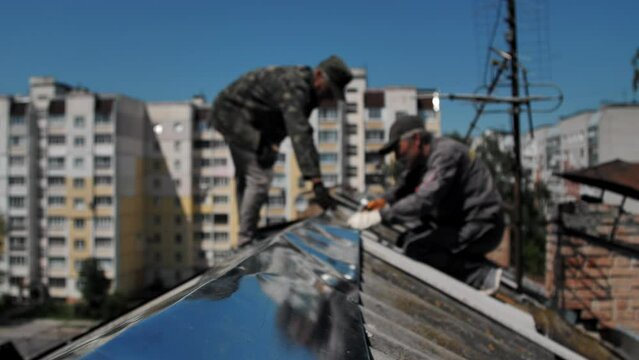 Residential building under construction. Repair of the roof of a multi-storey building. Two workers are working on the roof. Replacement of slate or other roofing materials.